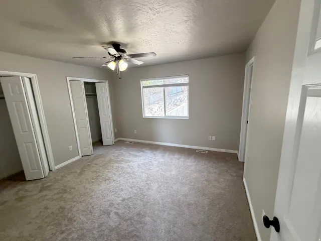 Carpeted flooring with dual bi-fold closet doors, a ceiling fan with integrated lighting, and a single window offering exterior scenery