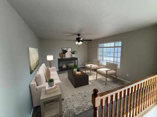 Spacious living area featuring light-toned walls, a ceiling fan, and a large window with blinds