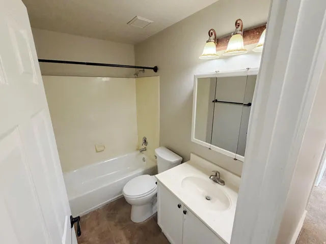 Bathroom featuring a white vanity with integrated sink, a medicine cabinet with mirrored doors, a three-light vanity fixture, and a built-in bathtub with shower