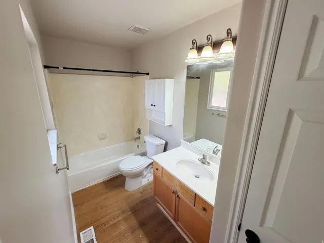 Wood-finish flooring with a white bathtub and shower surround