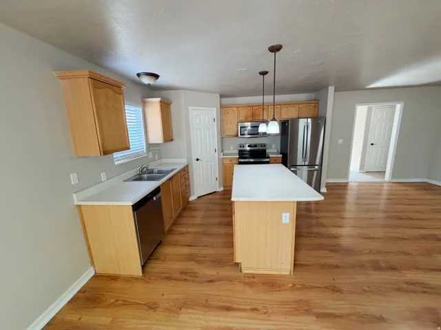 Kitchen featuring wood-finish flooring, light wood cabinetry, a center island with pendant lighting, stainless steel appliances, and light-toned countertops