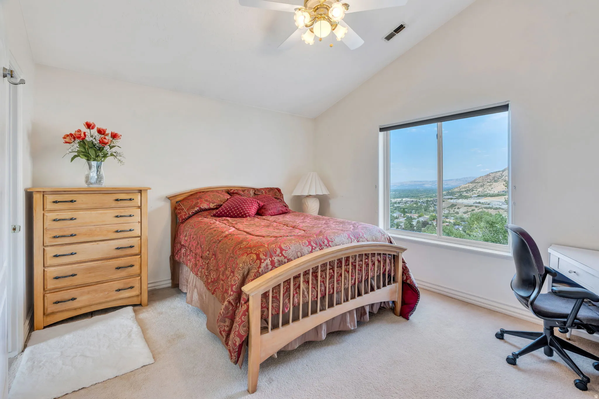 Bright secondary bedroom featuring a wood-frame bed, wood-finish dresser with multiple drawers, carpet flooring, and large picture window with expansive scenery