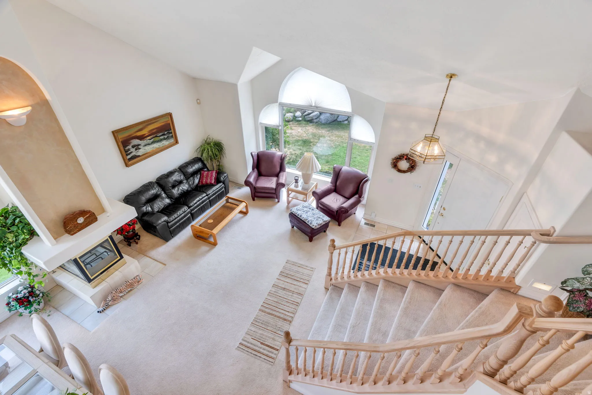 Two-story living area with vaulted ceilings, large arched windows, a built-in fireplace, and a grand staircase with wood balusters