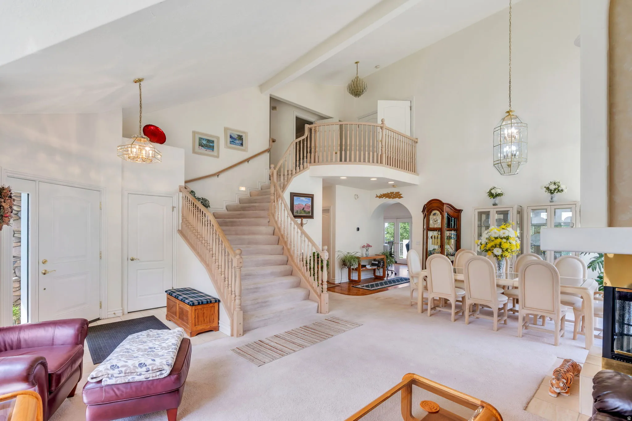 Soaring two-story foyer with natural light from multiple windows, grand staircase with wooden railings and balusters, and pendant lighting fixtures