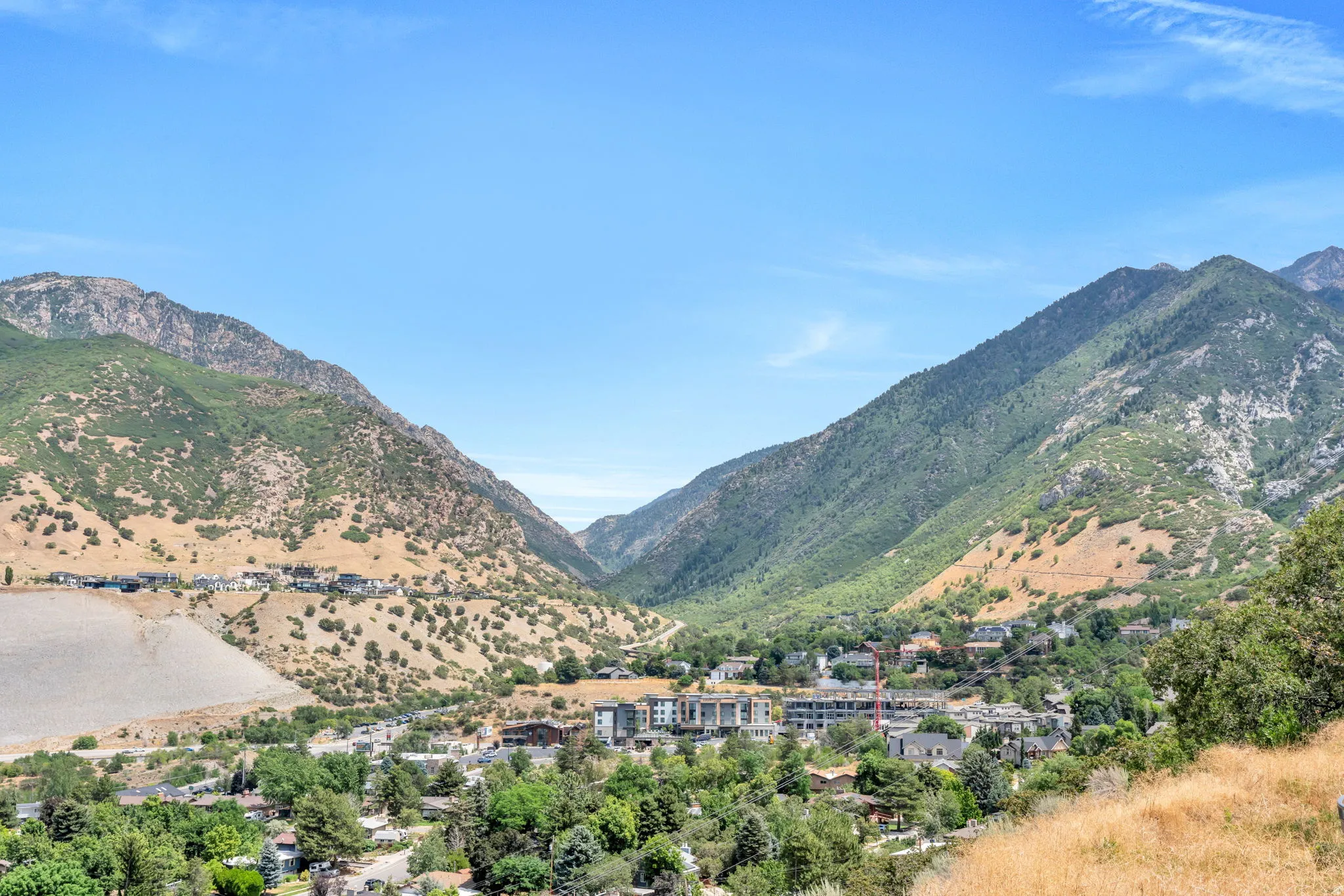 Expansive mountain landscape featuring a valley community with residential structures and established tree cover under a clear blue sky