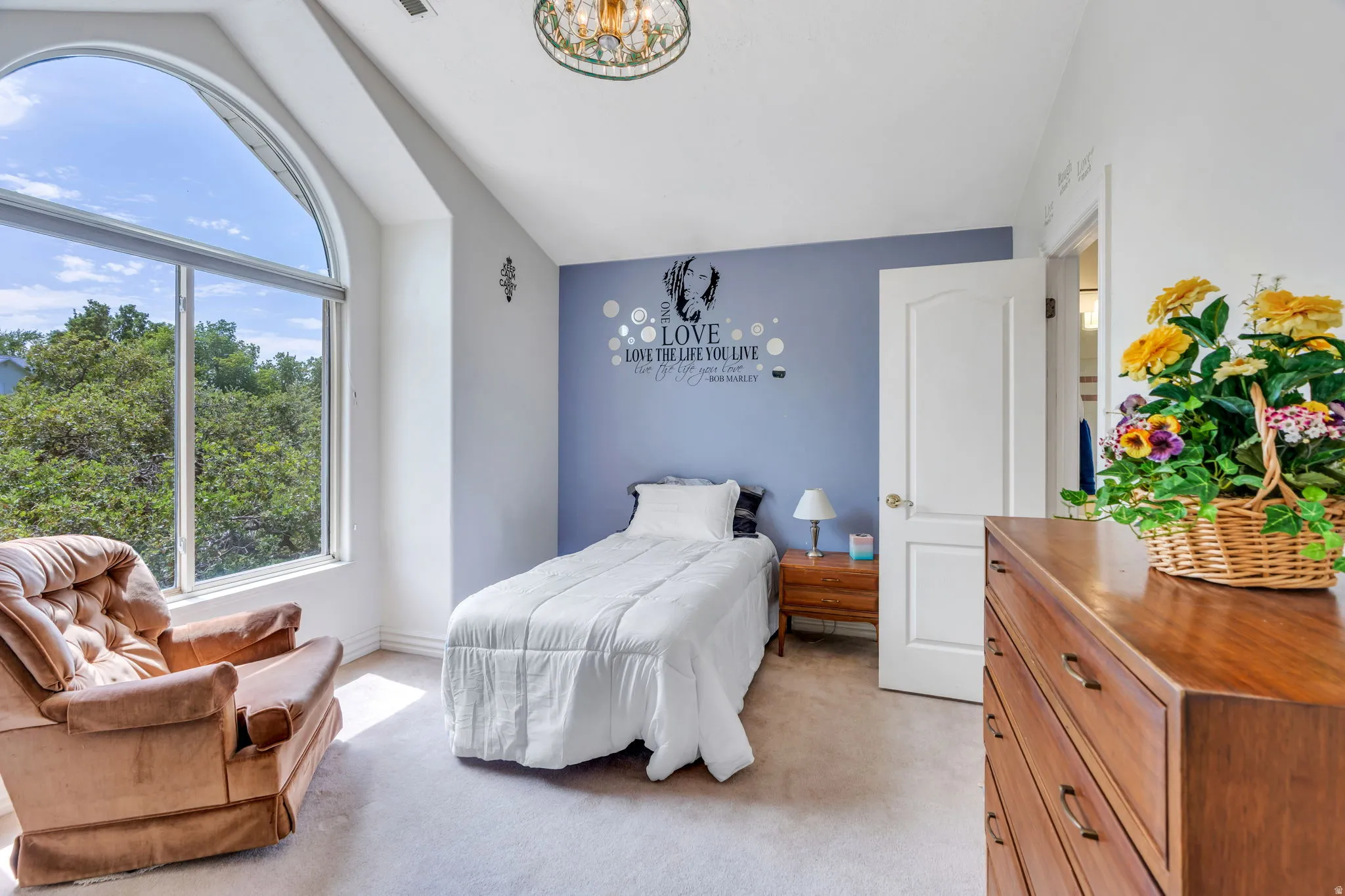 Room featuring an arched window, light-colored carpeting, a light blue accent wall, a white interior door, and a decorative ceiling light fixture