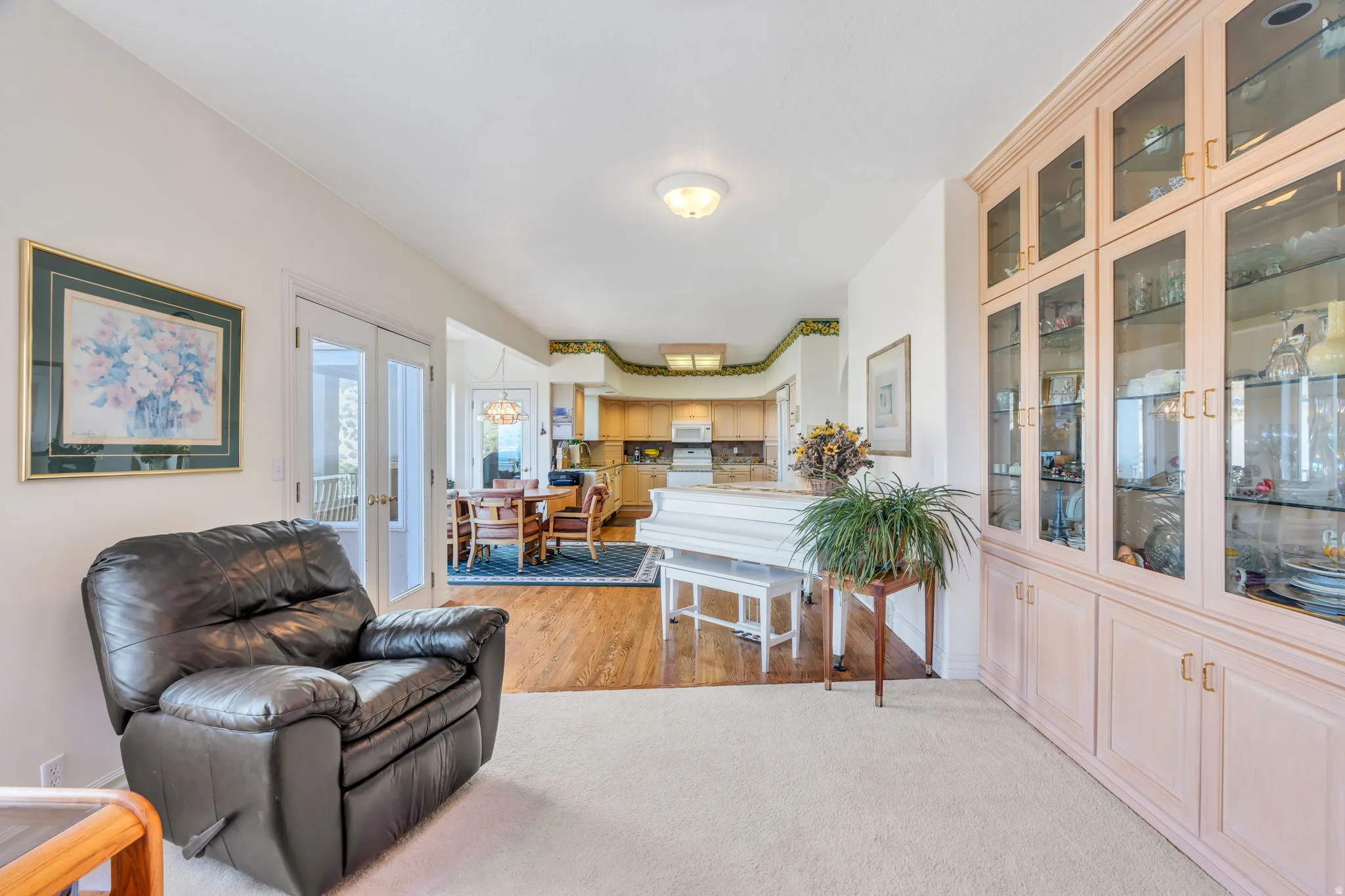 Open-concept living area featuring a built-in display cabinet with glass doors and polished hardware, recessed wall, and plush carpeting