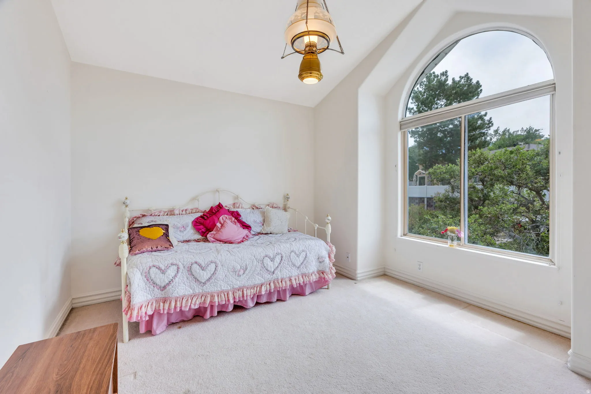 Spacious room featuring a large arched window, vaulted ceiling, and neutral-toned carpeting
