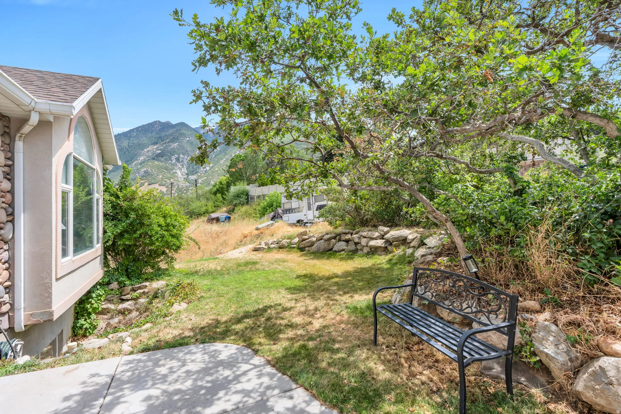 Terraced backyard with a patio slab, natural stone retaining wall, and mature trees