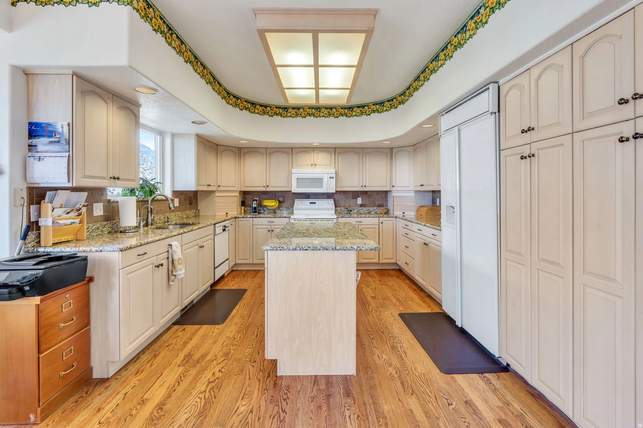 U-shaped kitchen featuring wood-finish flooring, a central island, light-toned cabinetry, granite countertops, and a built-in refrigerator