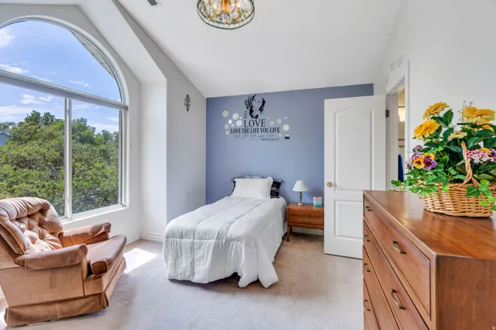 Room featuring an arched window, light-colored carpeting, a light blue accent wall, a white interior door, and a decorative ceiling light fixture