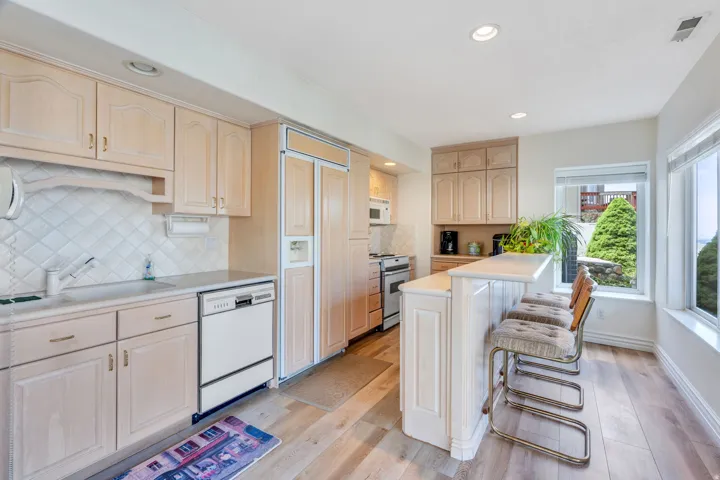 Bright, open kitchen showcasing light wood cabinetry, stainless steel appliances, and a large island with seating
