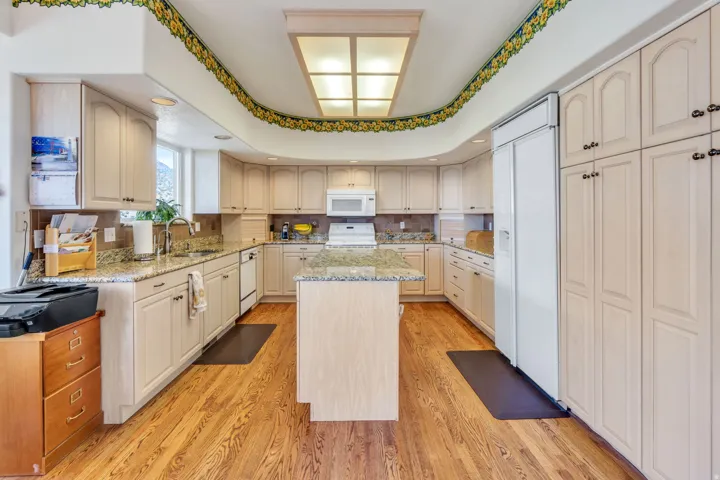 U-shaped kitchen featuring wood-finish flooring, a central island, light-toned cabinetry, granite countertops, and a built-in refrigerator