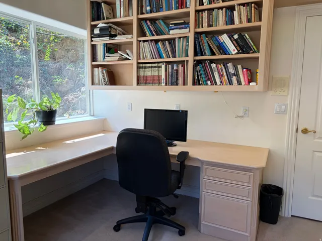 Built-in L-shaped desk with integrated drawer storage, large window, and custom overhead shelving