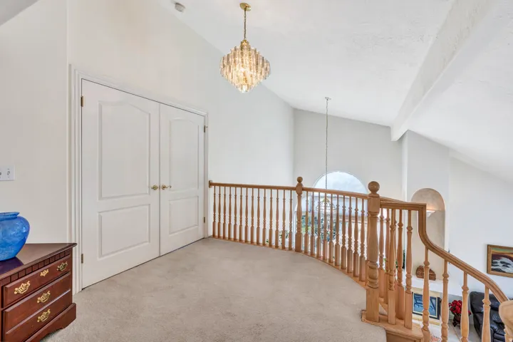 Vaulted ceiling with an ornate chandelier, arched transom window, painted double doors, and a wood-finish railing