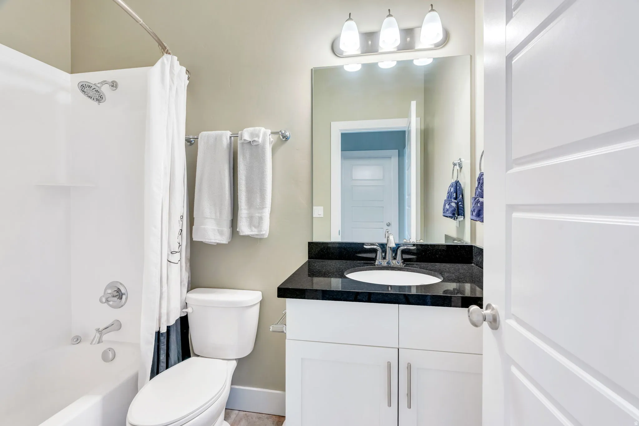 Bathroom featuring a white tub and shower combination, a single vanity with a dark countertop and undermount sink, white cabinetry, and a chrome light fixture