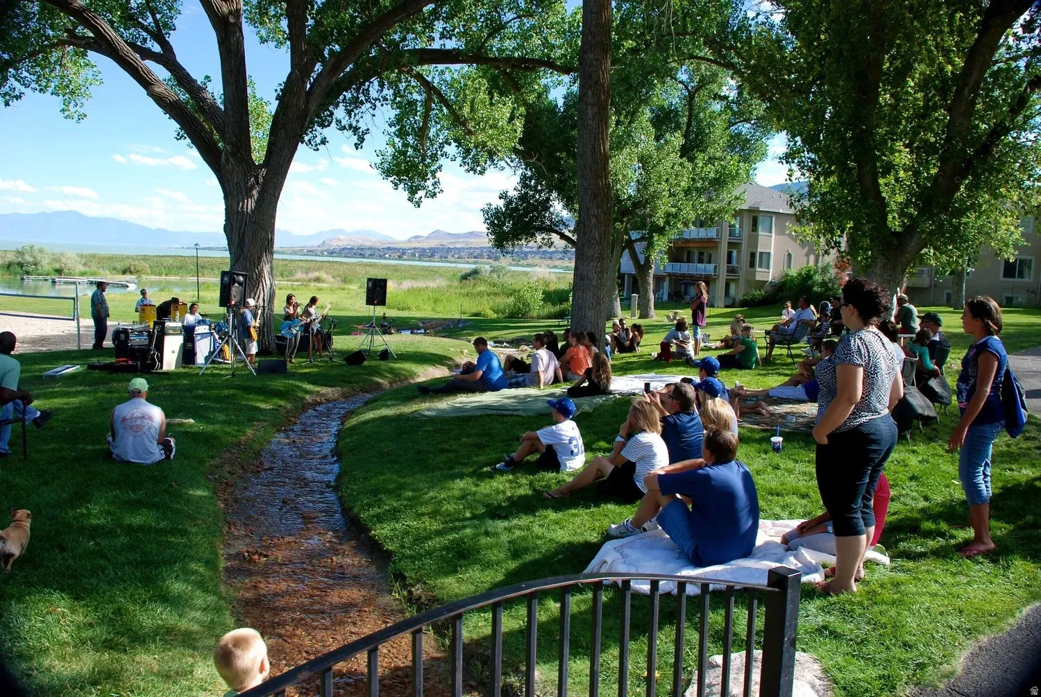 Expansive green space featuring a natural water feature, mature shade trees, and mountain scenery