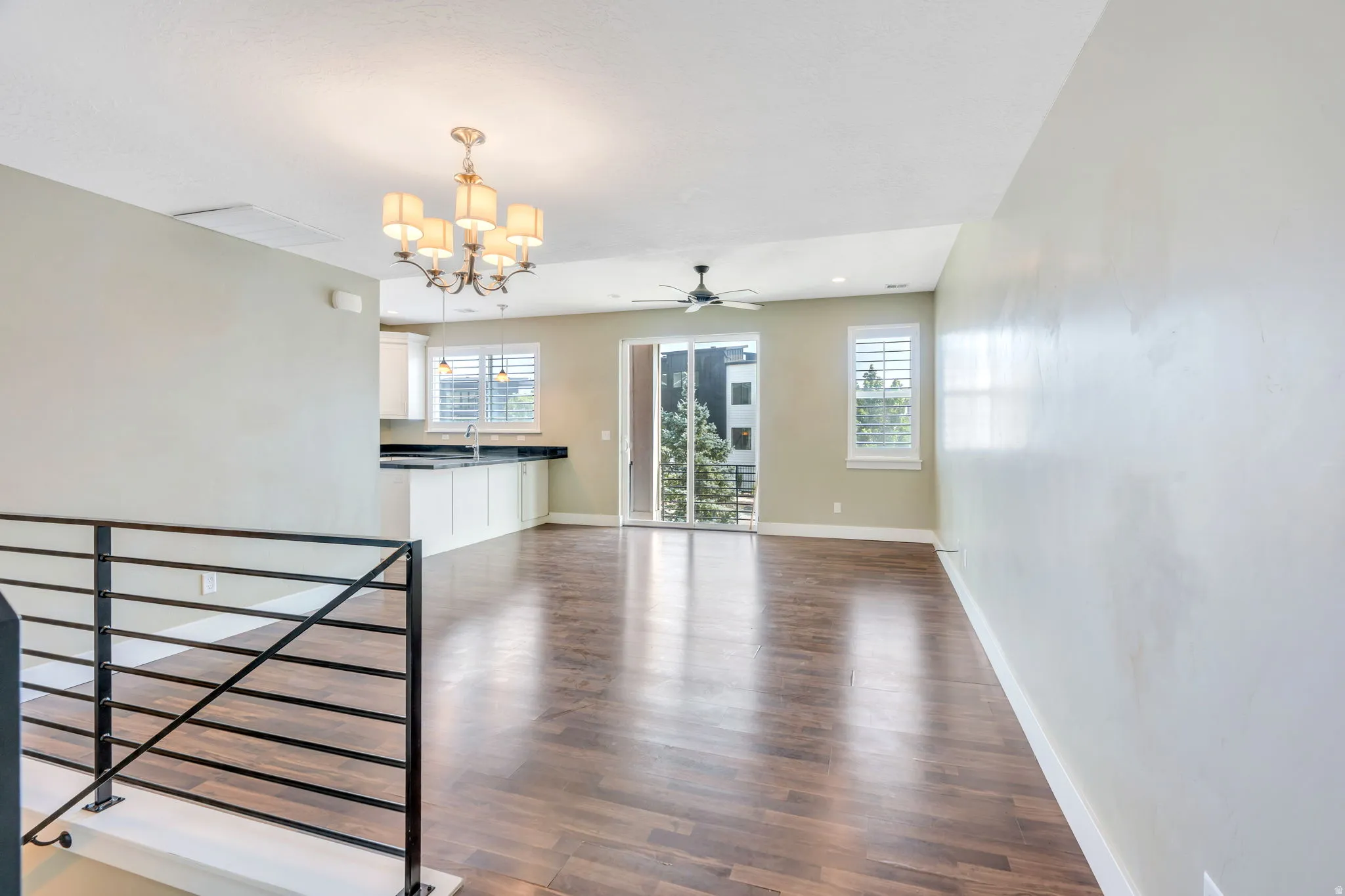 Spacious main living area featuring dark wood-finish flooring, a contemporary chandelier, a ceiling fan, and a sliding glass door leading to a balcony