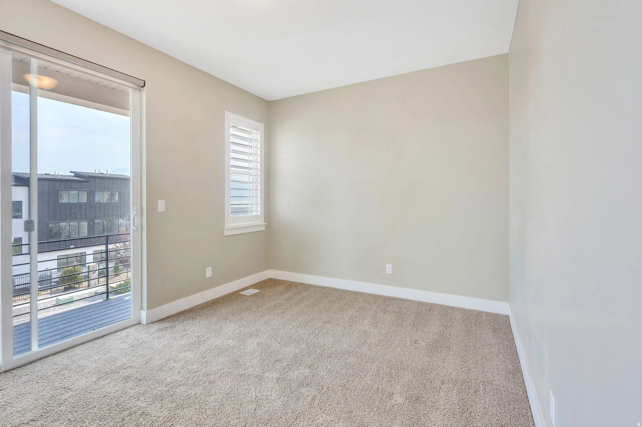Neutral-toned carpeted room featuring a sliding glass door opening to an exterior balcony