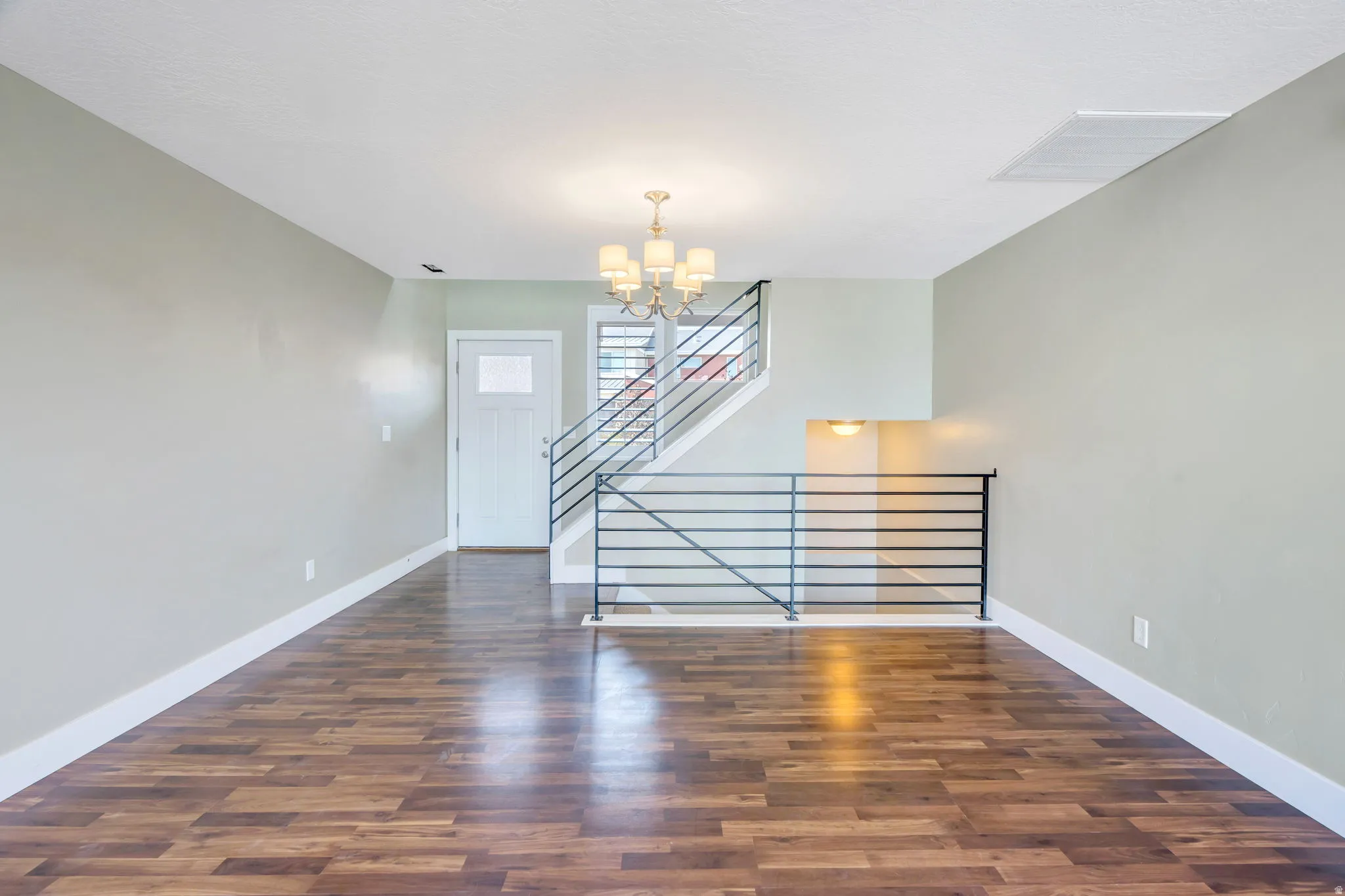 Spacious room featuring wood-finish flooring, light-toned walls, and a modern chandelier
