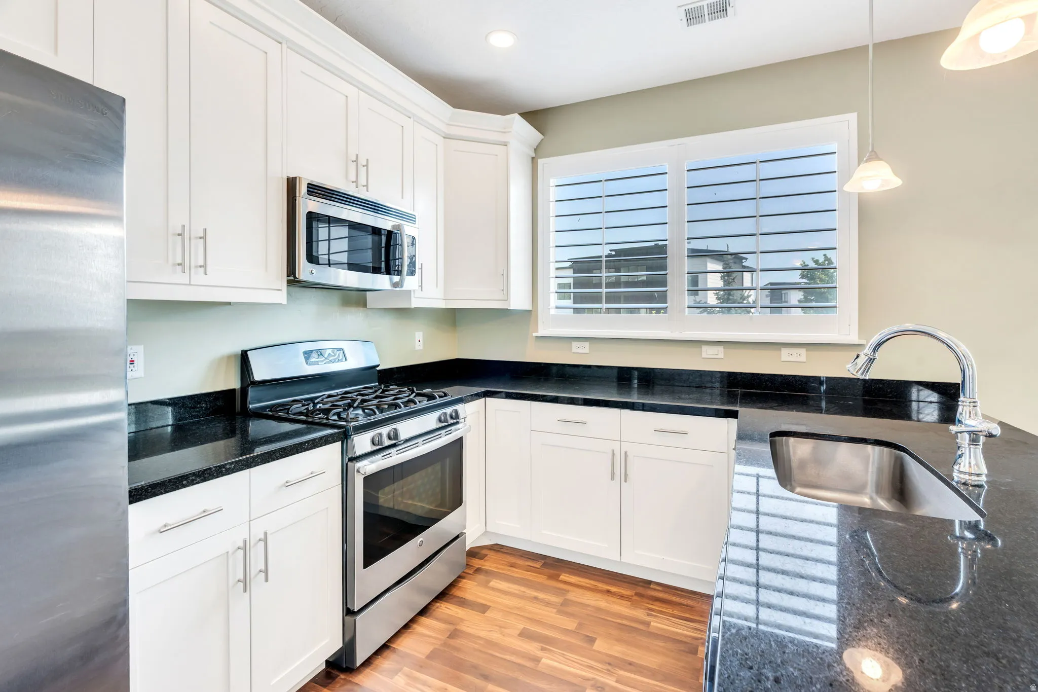 Kitchen featuring white shaker cabinetry, stainless steel appliances, black countertops, and wood-finish flooring