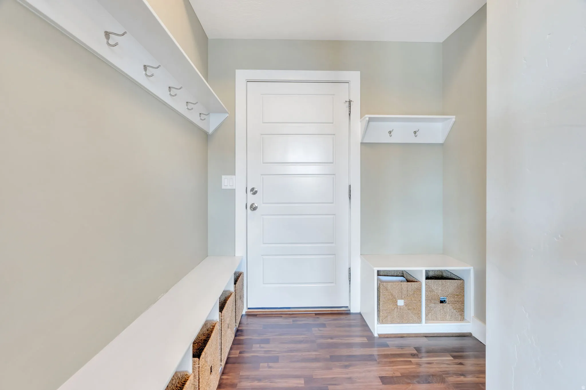 Entryway with wood-finish flooring, a white paneled door, and built-in white shelving with integrated hooks