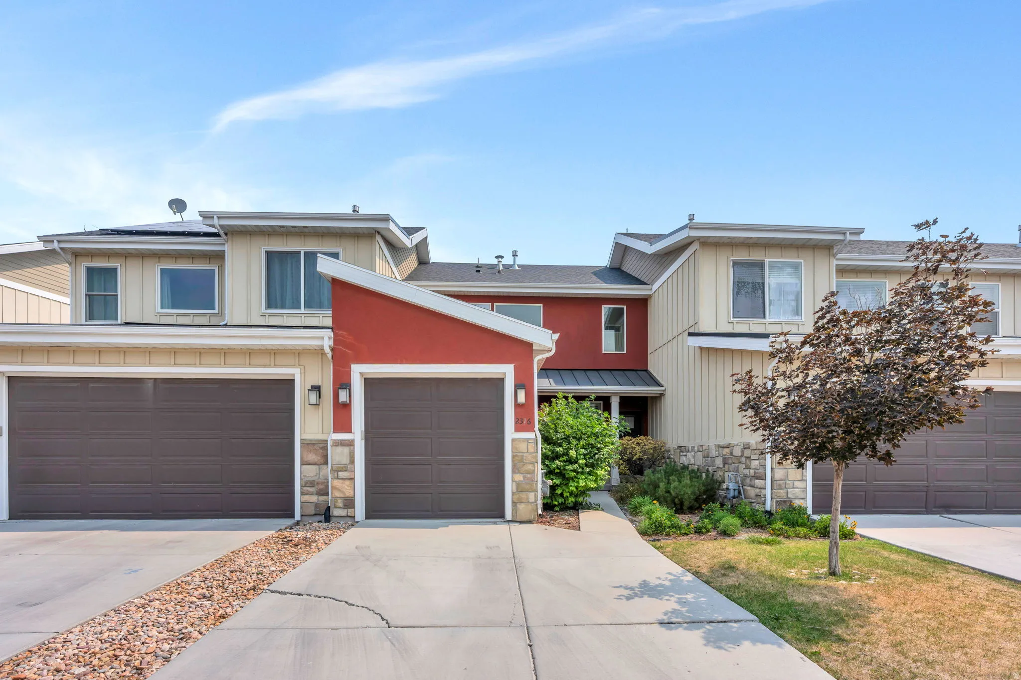 Contemporary multi-level exterior with a striking red accent wall, light beige siding, and stone façade detailing