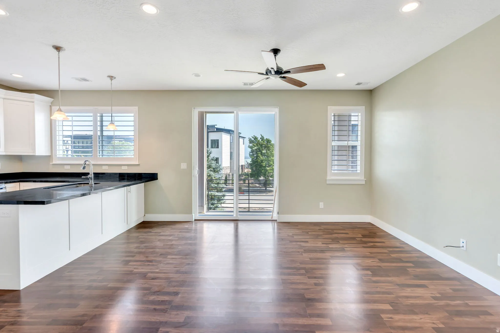 Open-concept living area featuring wood-finish flooring, a kitchen island with dark stone countertop, white cabinetry, and recessed lighting