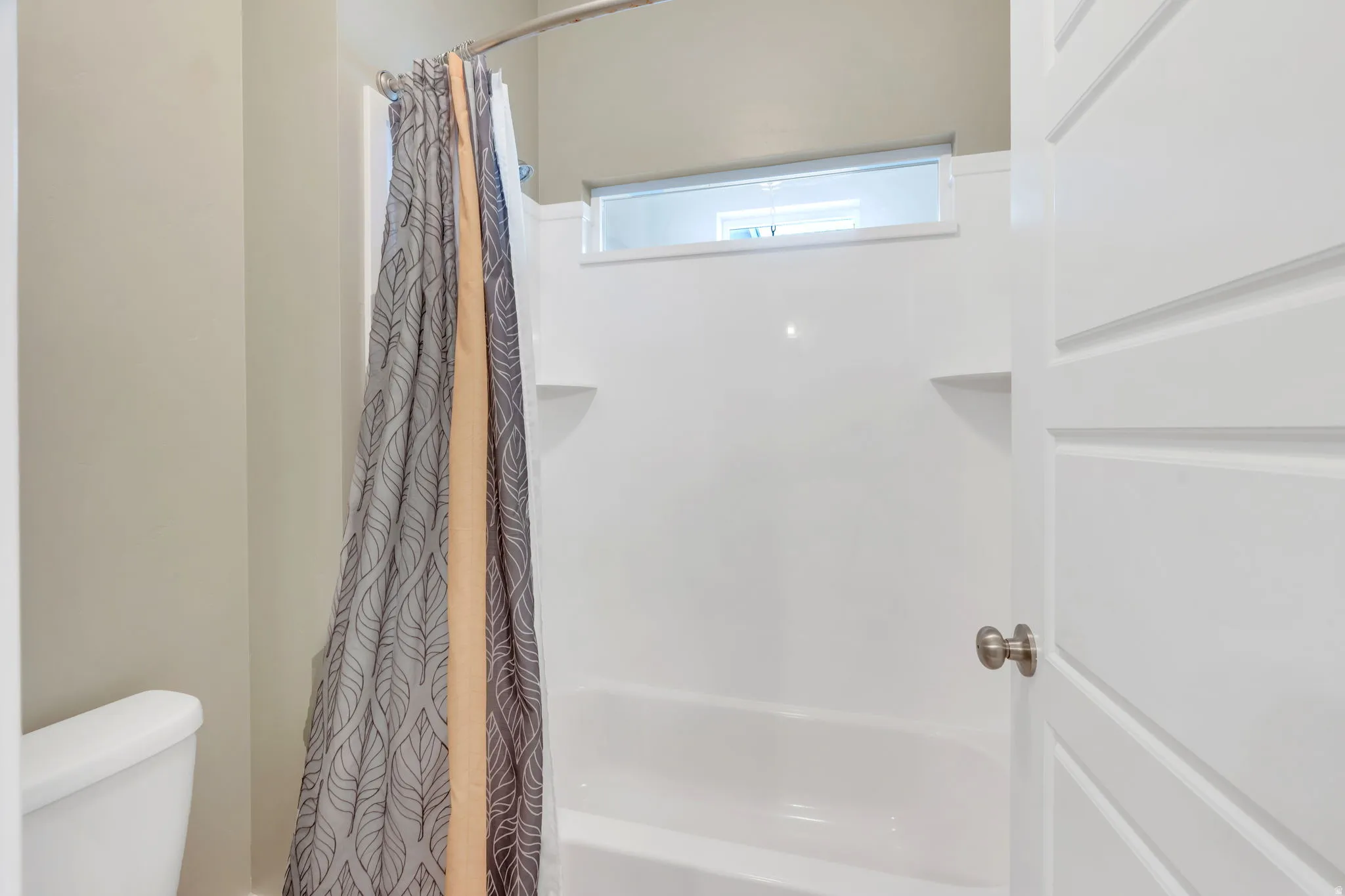 White shower-over-tub combination with built-in shelving, opaque transom window, and brushed nickel hardware