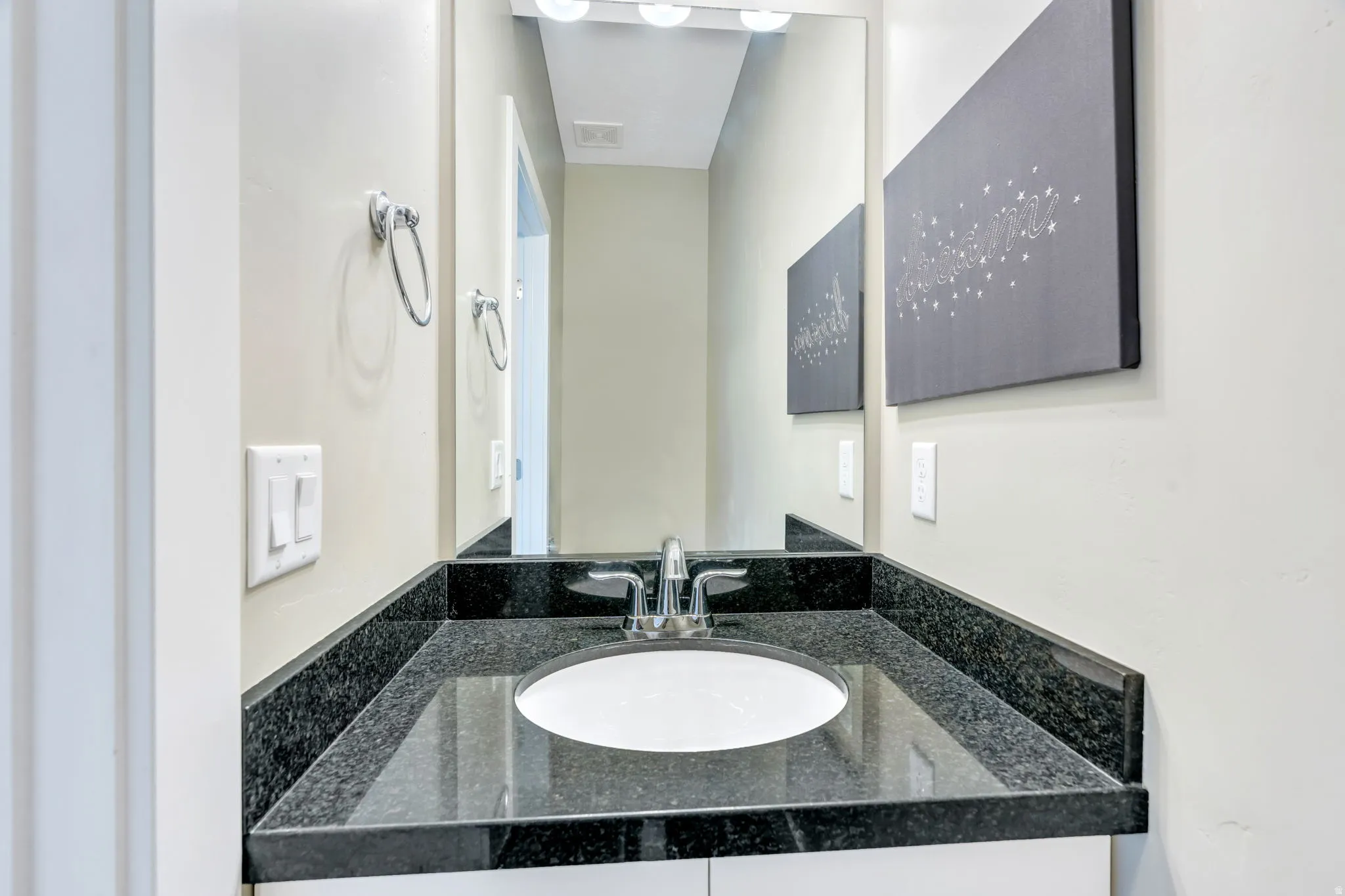 Bathroom vanity featuring a polished dark speckled countertop, undermount sink, and chrome faucet