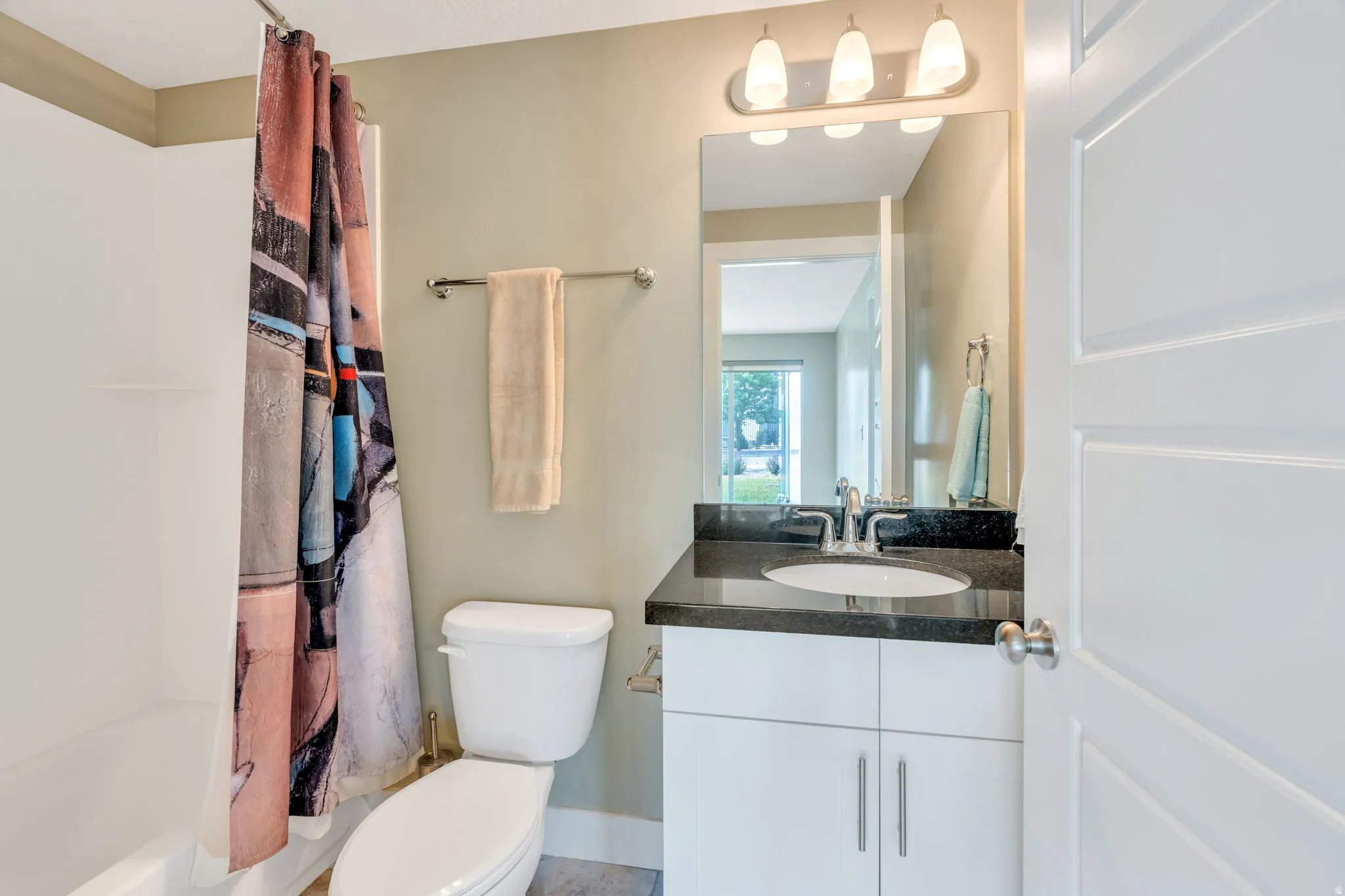 Bathroom featuring a white tub, toilet, and a vanity with a dark countertop and undermount sink