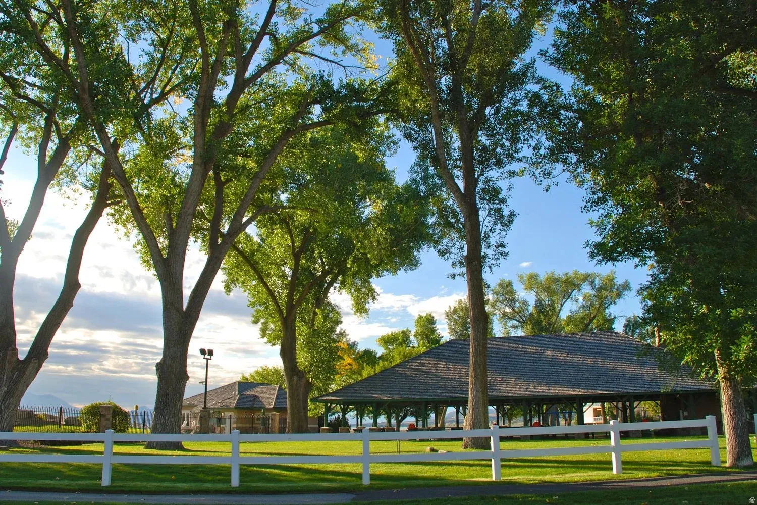 Expansive green lawn framed by mature trees, featuring a white picket fence
