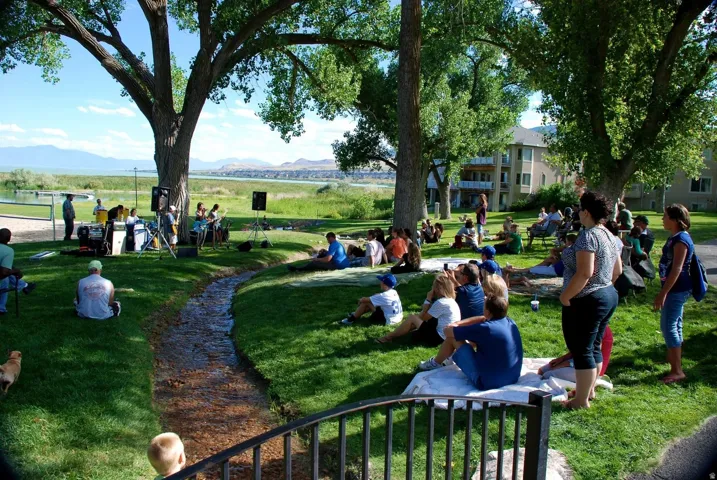 Expansive green space featuring a natural water feature, mature shade trees, and mountain scenery