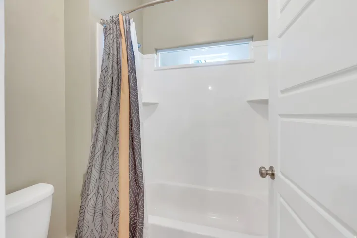White shower-over-tub combination with built-in shelving, opaque transom window, and brushed nickel hardware