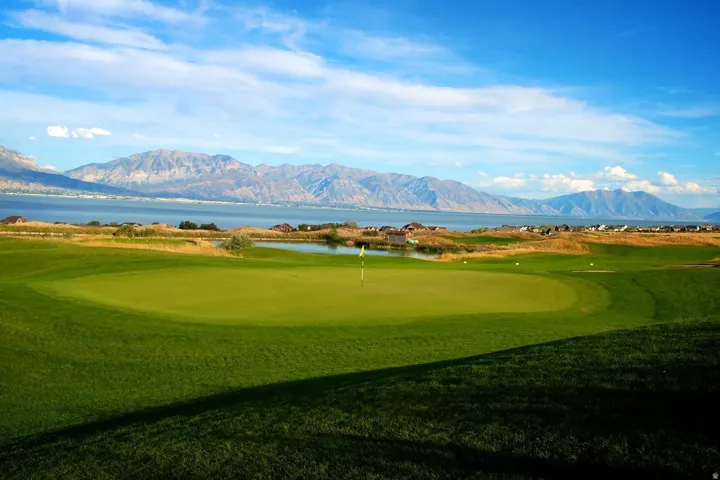 Manicured golf course green with a white flag, surrounded by a water feature and distant mountains