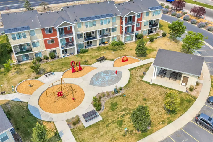 Multifamily residential building featuring balconies, a covered outdoor gathering area, and a playground with benches and various play structures