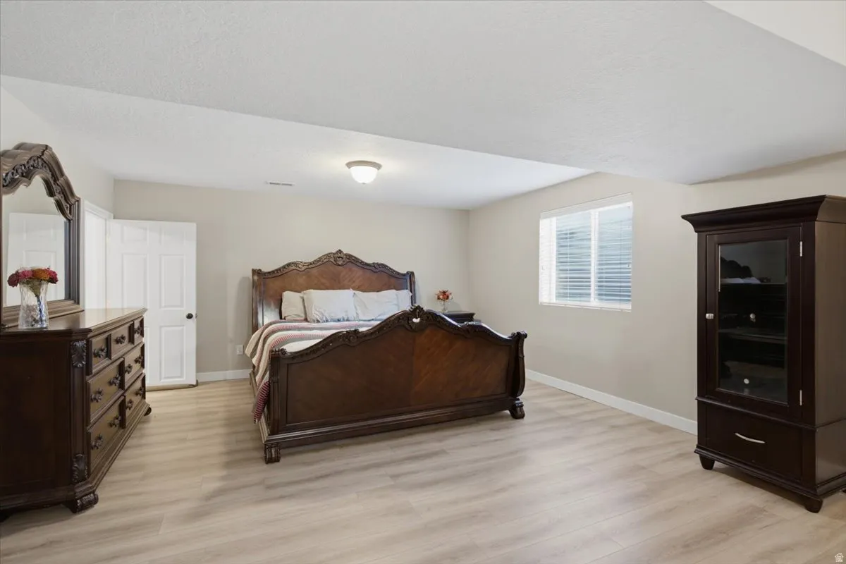 Massive Primary Basement Master, Spacious room featuring light wood-finish flooring, neutral wall tones, and a window with blinds