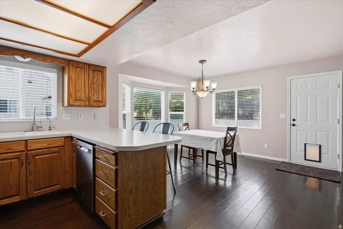 Kitchen and dining area featuring wood-finish cabinetry, a stainless steel dishwasher, and a breakfast bar with a solid surface countertop