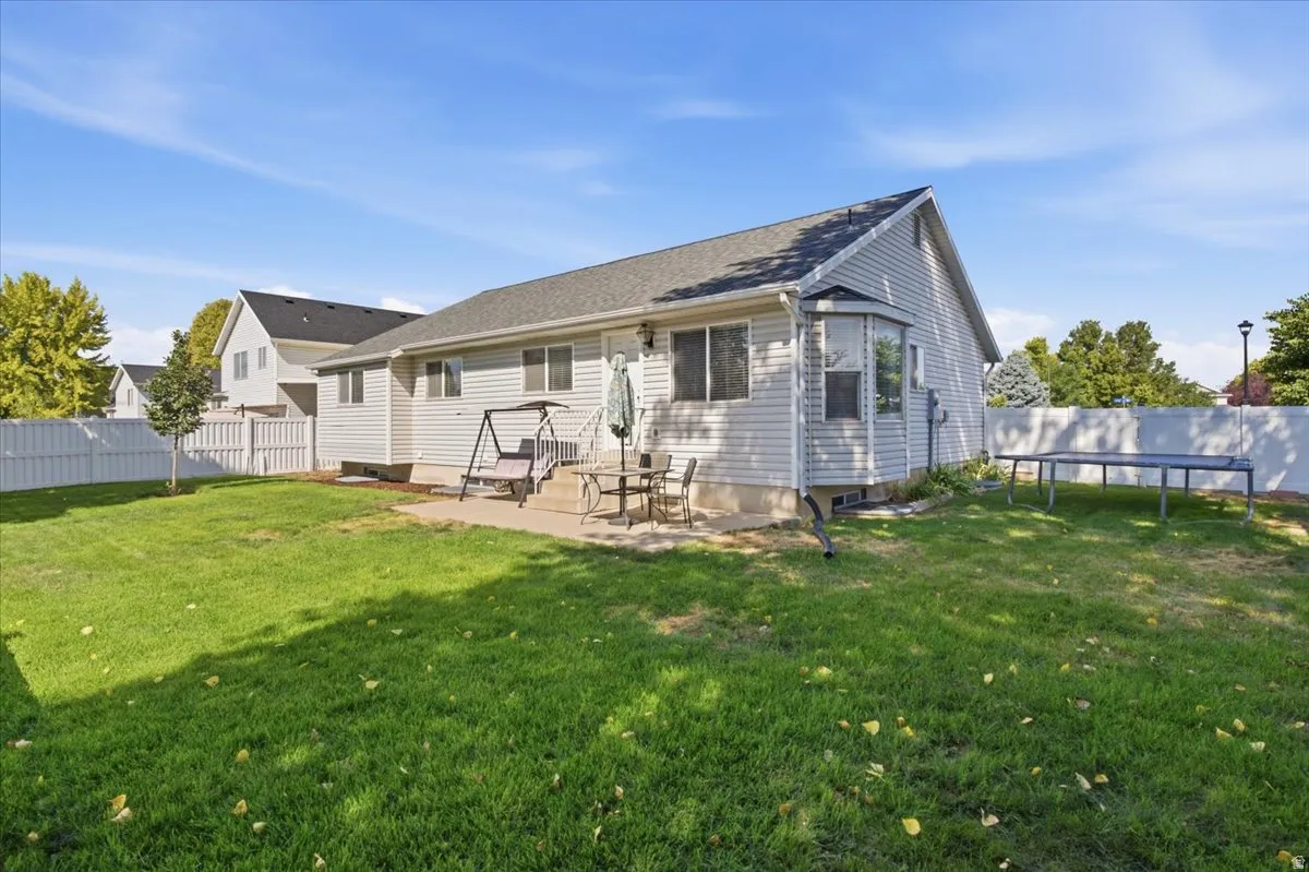 Spacious backyard featuring a concrete patio, light-toned siding, bay window, and white privacy fencing