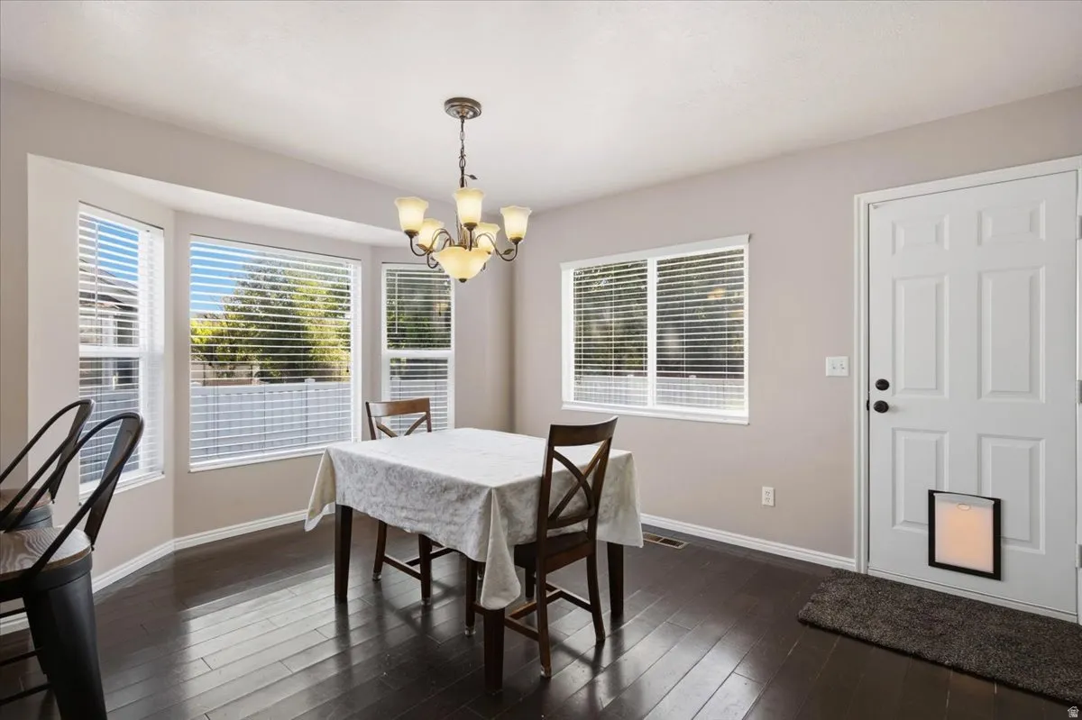 Dining space featuring rich dark wood-finish flooring, a bay window with blinds, an overhead chandelier, and a white paneled door