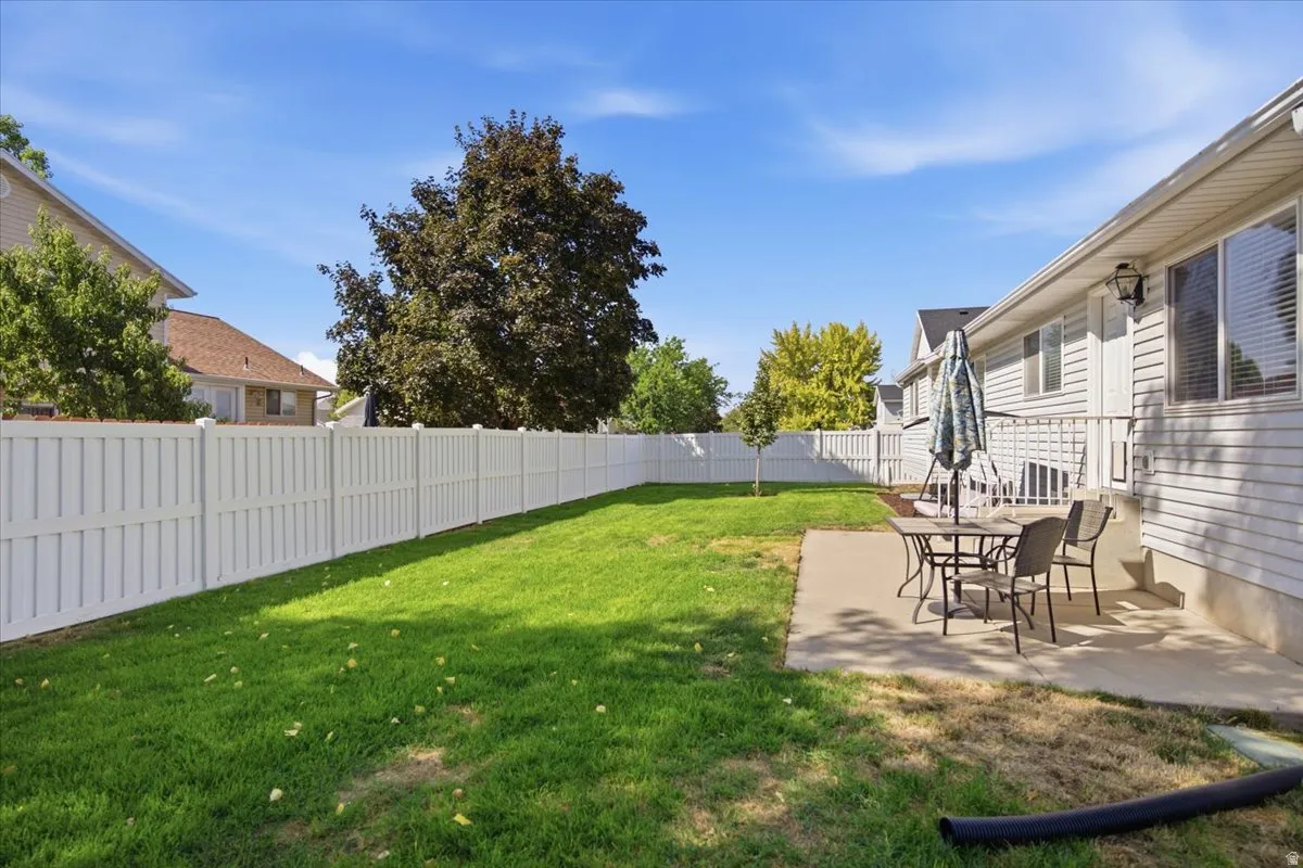 Spacious backyard featuring a manicured lawn, full privacy fencing, and a concrete patio