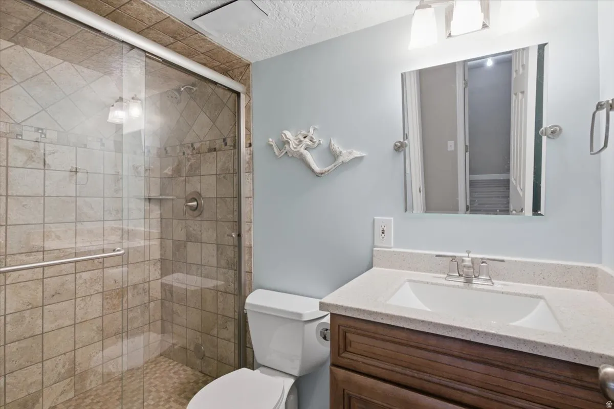 Bathroom featuring a glass-enclosed shower with tile surround, a single vanity with an integrated sink and light-toned countertop, and a built-in toilet