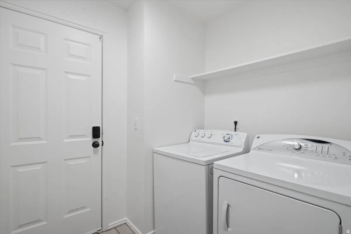 Dedicated laundry area featuring a white six-panel door, light-colored walls, and an overhead storage shelf