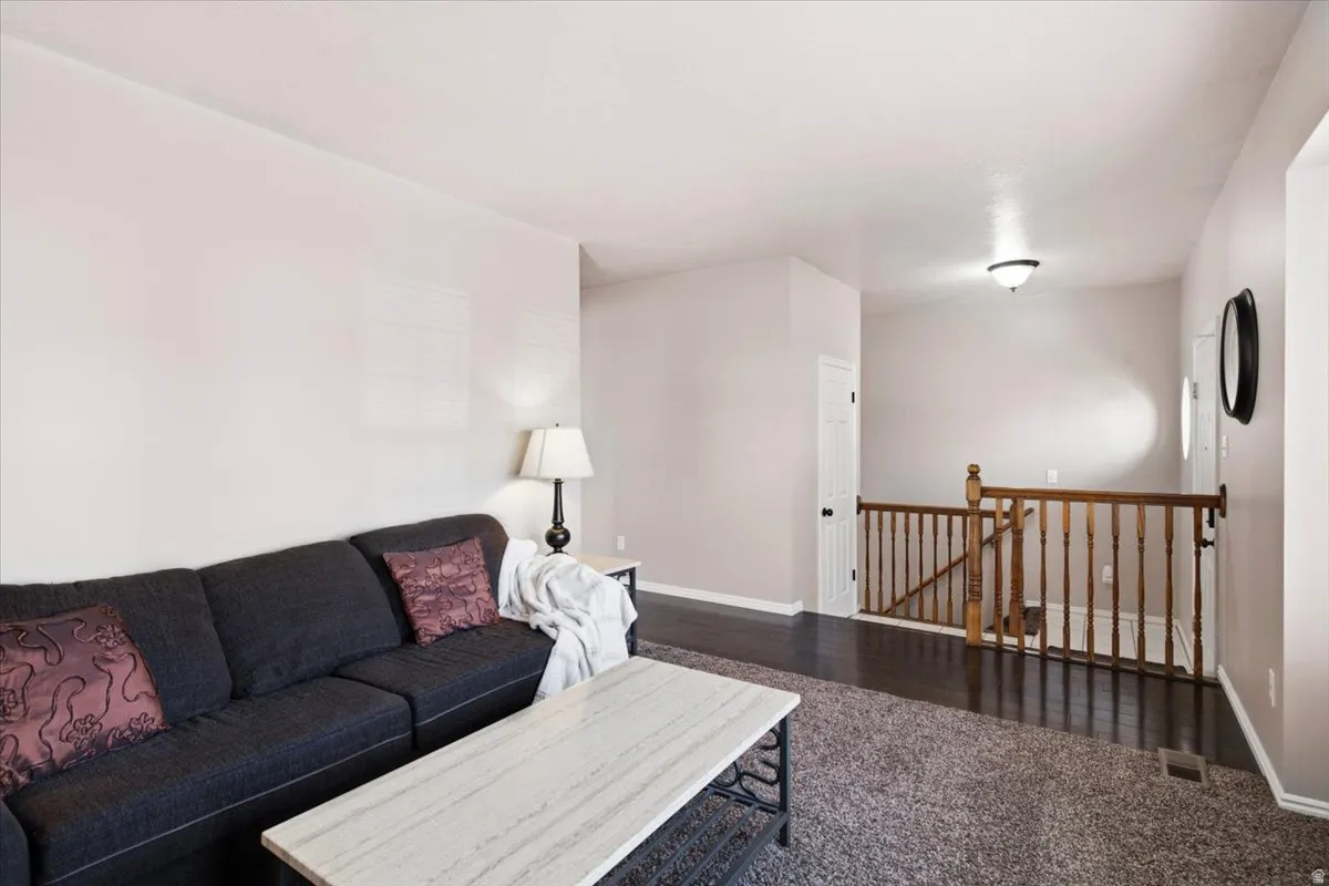 Carpeted living area featuring light-toned walls, contrasting dark wood-finish flooring, and a wooden banister