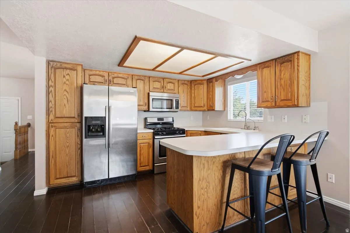 Kitchen featuring wood cabinetry, stainless steel appliances, white countertops, and dark wood-finish flooring