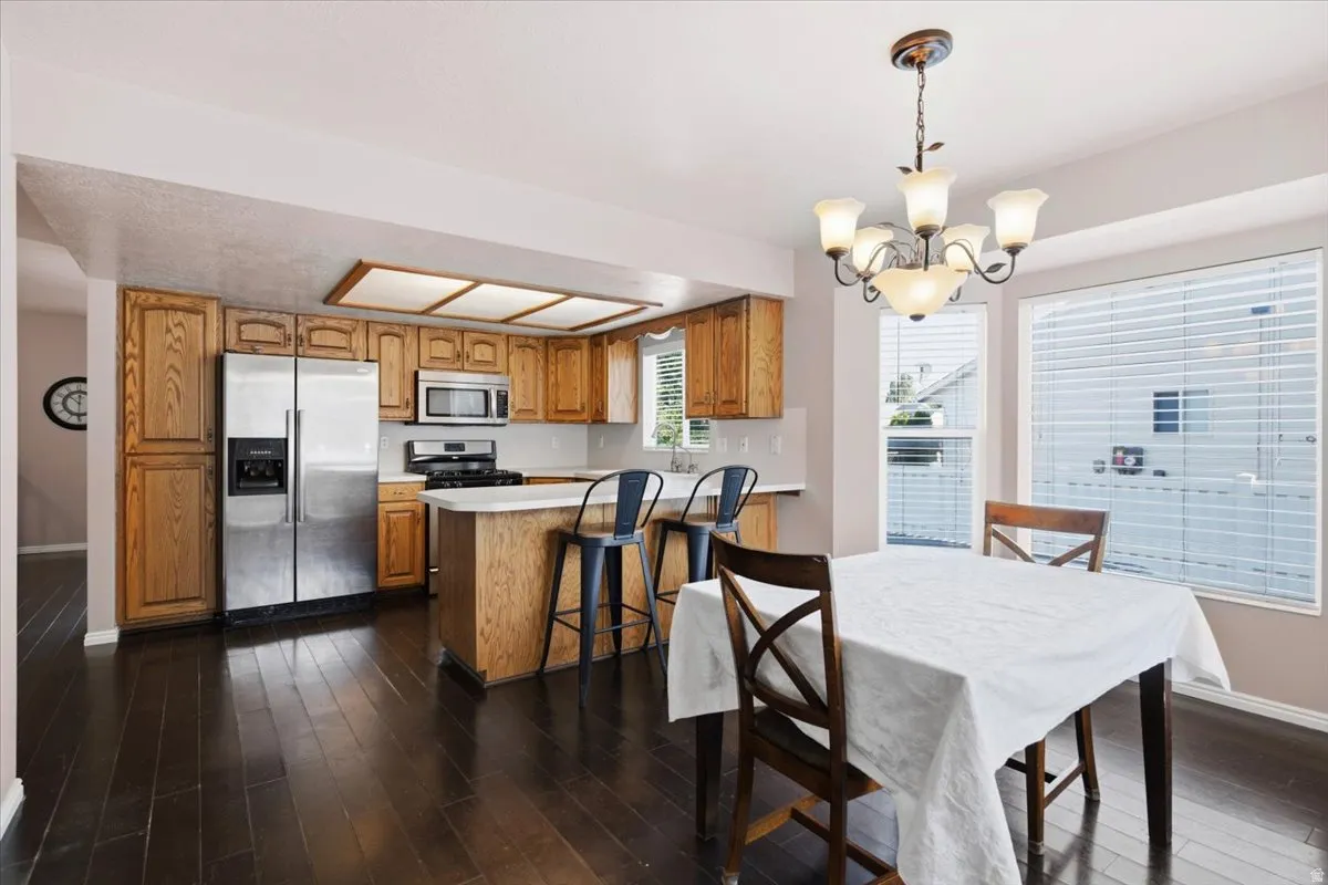 Kitchen and dining area featuring dark wood-finish flooring, light wood cabinetry, stainless steel appliances, and a central island with bar seating