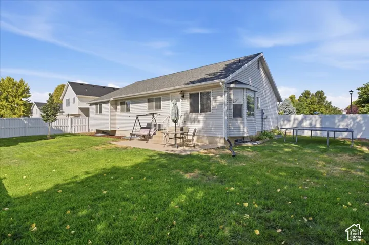 Spacious backyard featuring a concrete patio, light-toned siding, bay window, and white privacy fencing