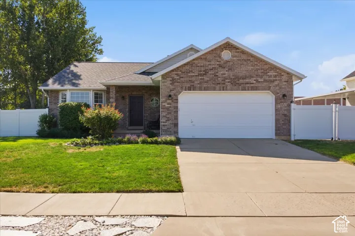 Brick facade residence featuring an attached two-car garage, a concrete driveway, and a white vinyl fence