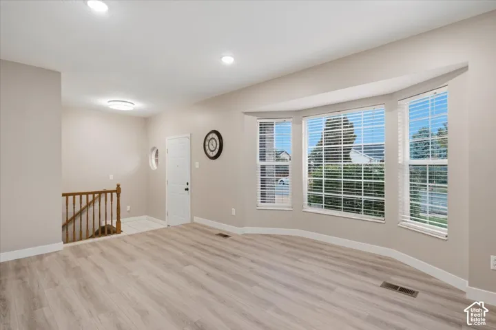 Living area featuring wood-finish flooring, a three-panel bay window, recessed lighting, and a wood-railing staircase