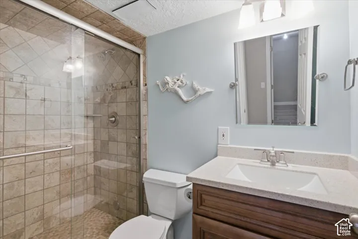 Bathroom featuring a glass-enclosed shower with tile surround, a single vanity with an integrated sink and light-toned countertop, and a built-in toilet